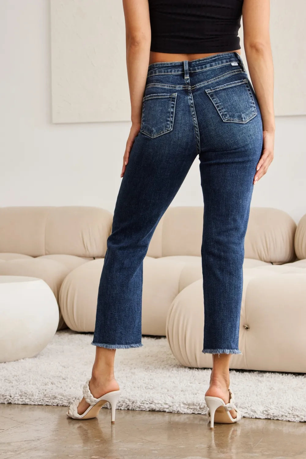 High-waist dark wash jeans with raw frayed hems and knee distress