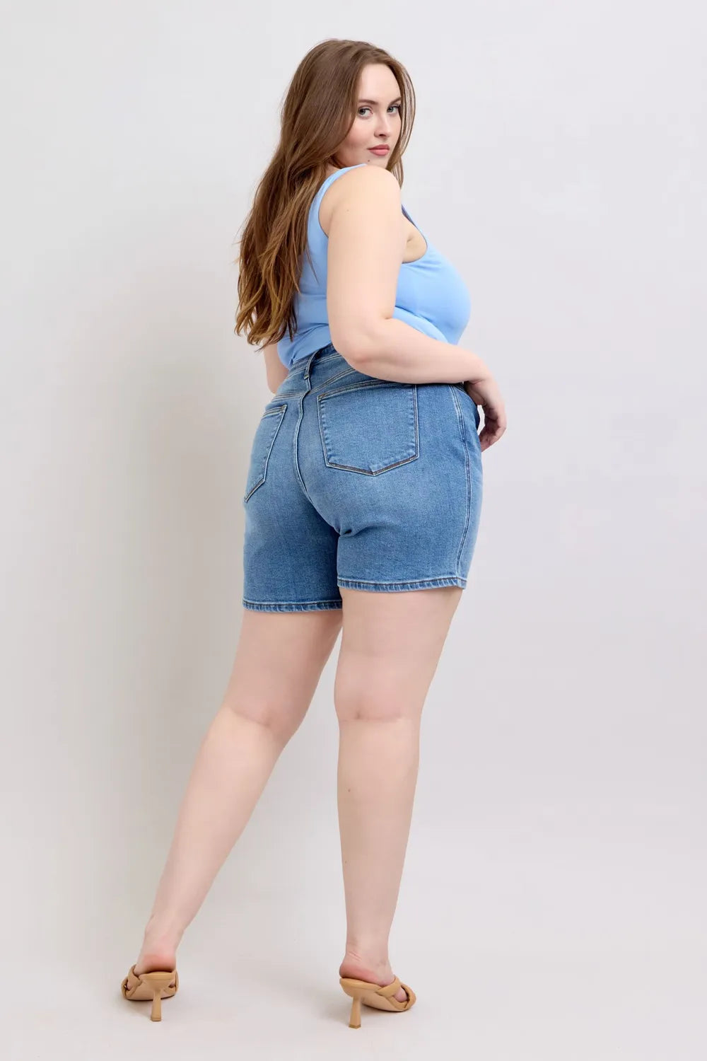 3/4 back view: medium-wash denim shorts with rear pockets and belt loops