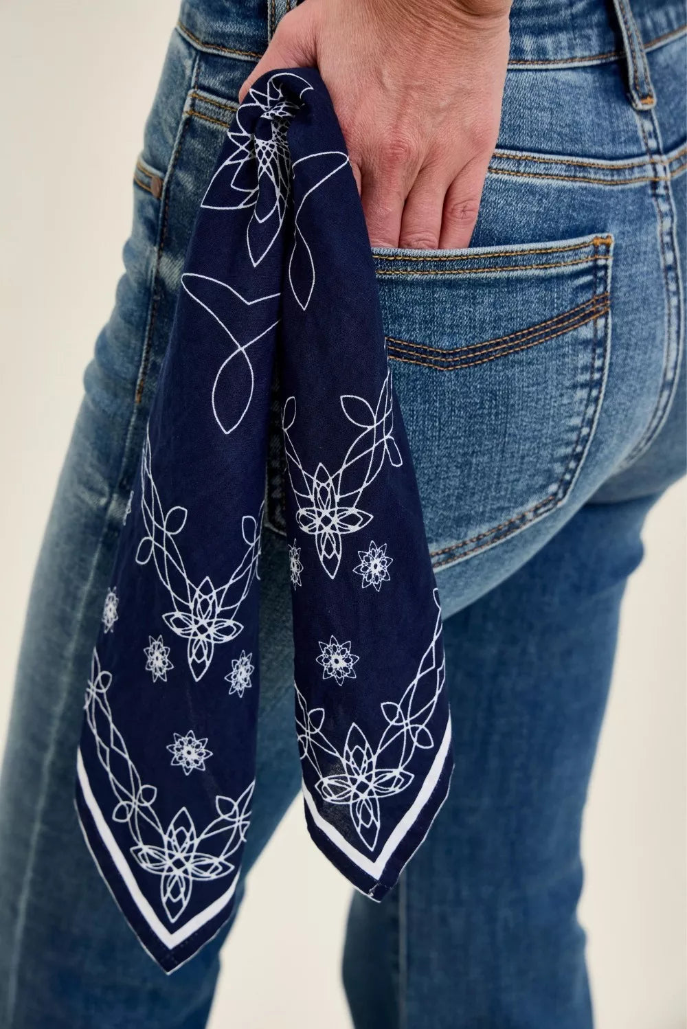 Navy bandana loop with white pattern scarf next to the jeans back pocket