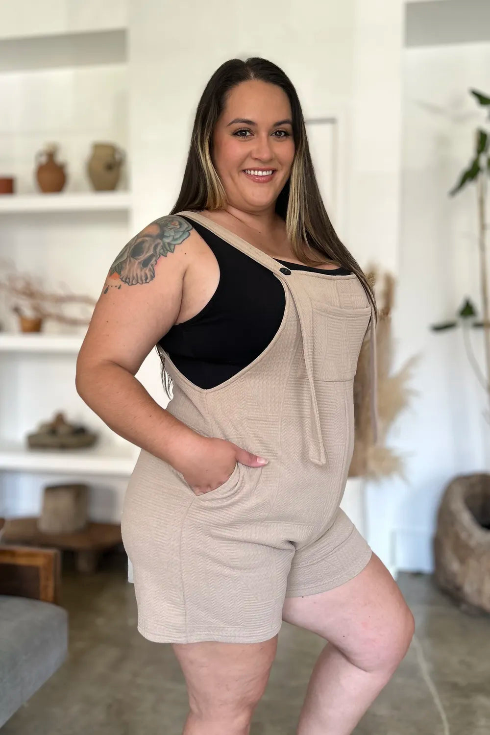 Beige textured sleeveless romper with wide straps and button detail on bib front