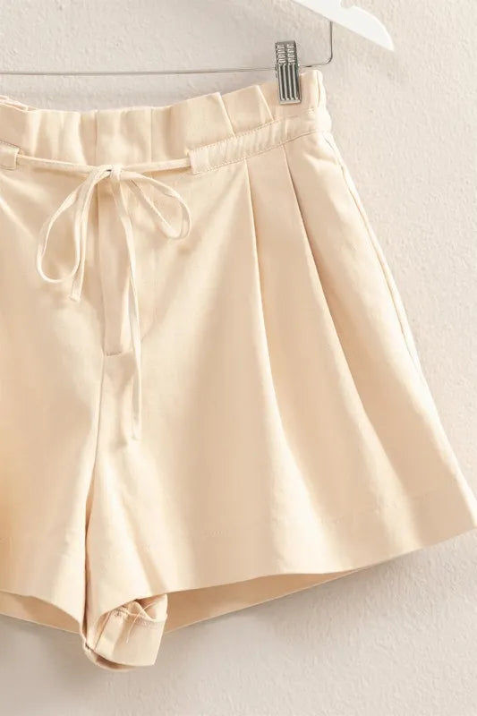 Oatmeal paperbag shorts close-up, tie at waistband with pleated panels