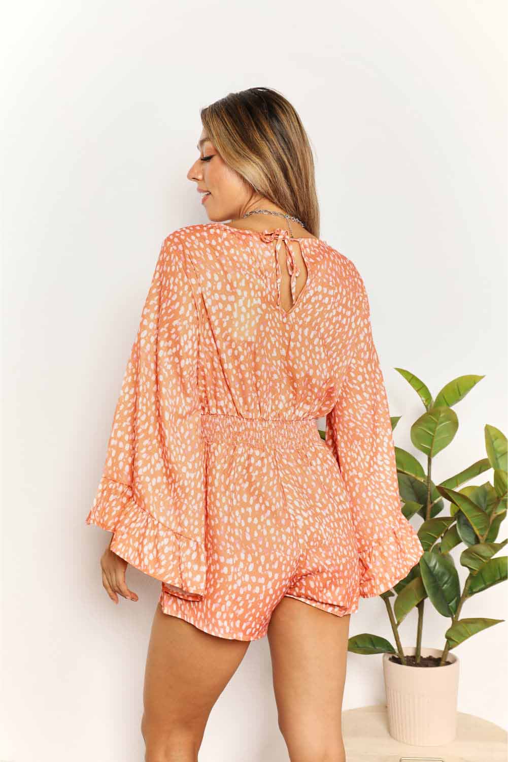 Back view: tangerine printed surplice romper with tie at open neckline