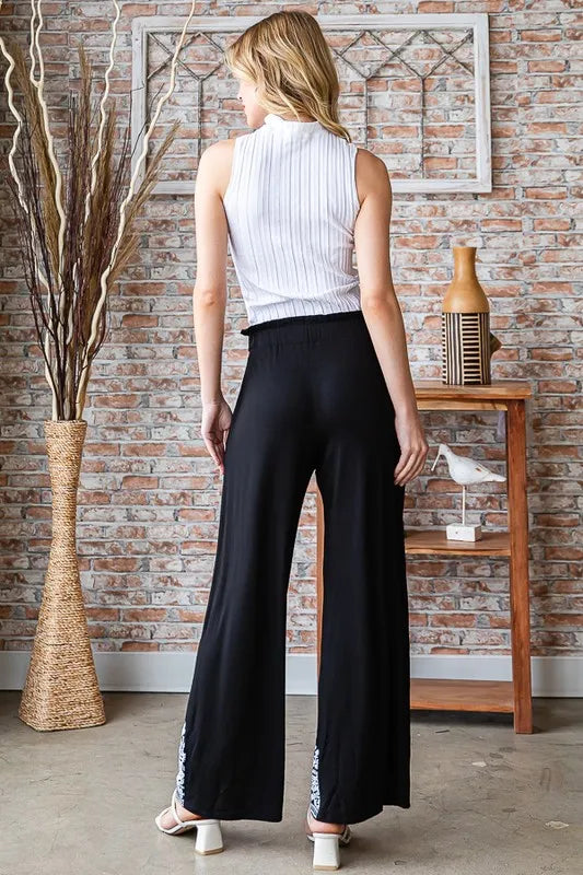 Back view of black wide-leg pants with elastic waist and patterned hem border