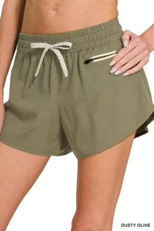 Dusty olive lined shorts with elastic waist, drawstring ties, and zip coin pocket