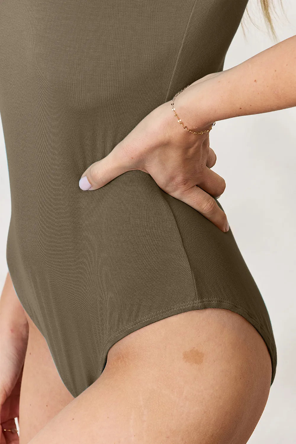 Olive bodysuit fabric close-up at waist seam and high leg opening