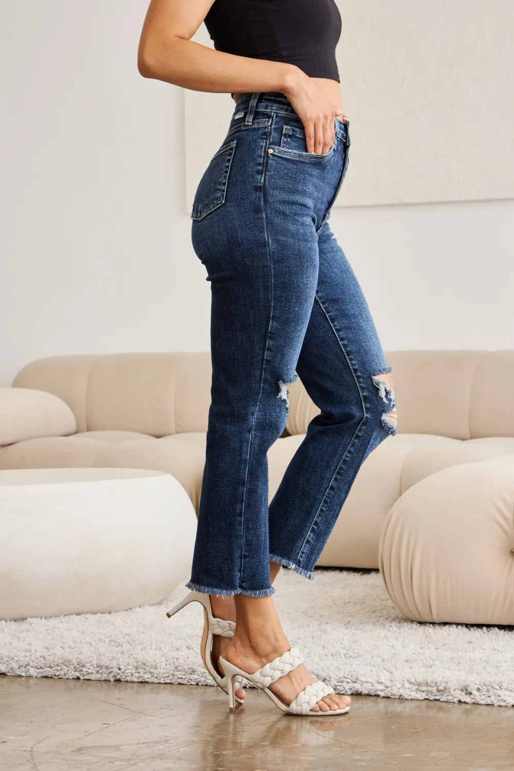 High-waist dark denim jeans with raw frayed cuffs and ripped knee patches