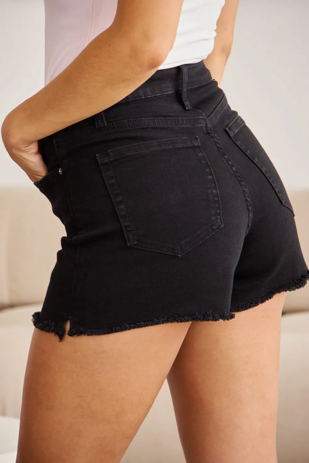 Black denim shorts close-up of front pocket, stitching, and frayed bottom hem