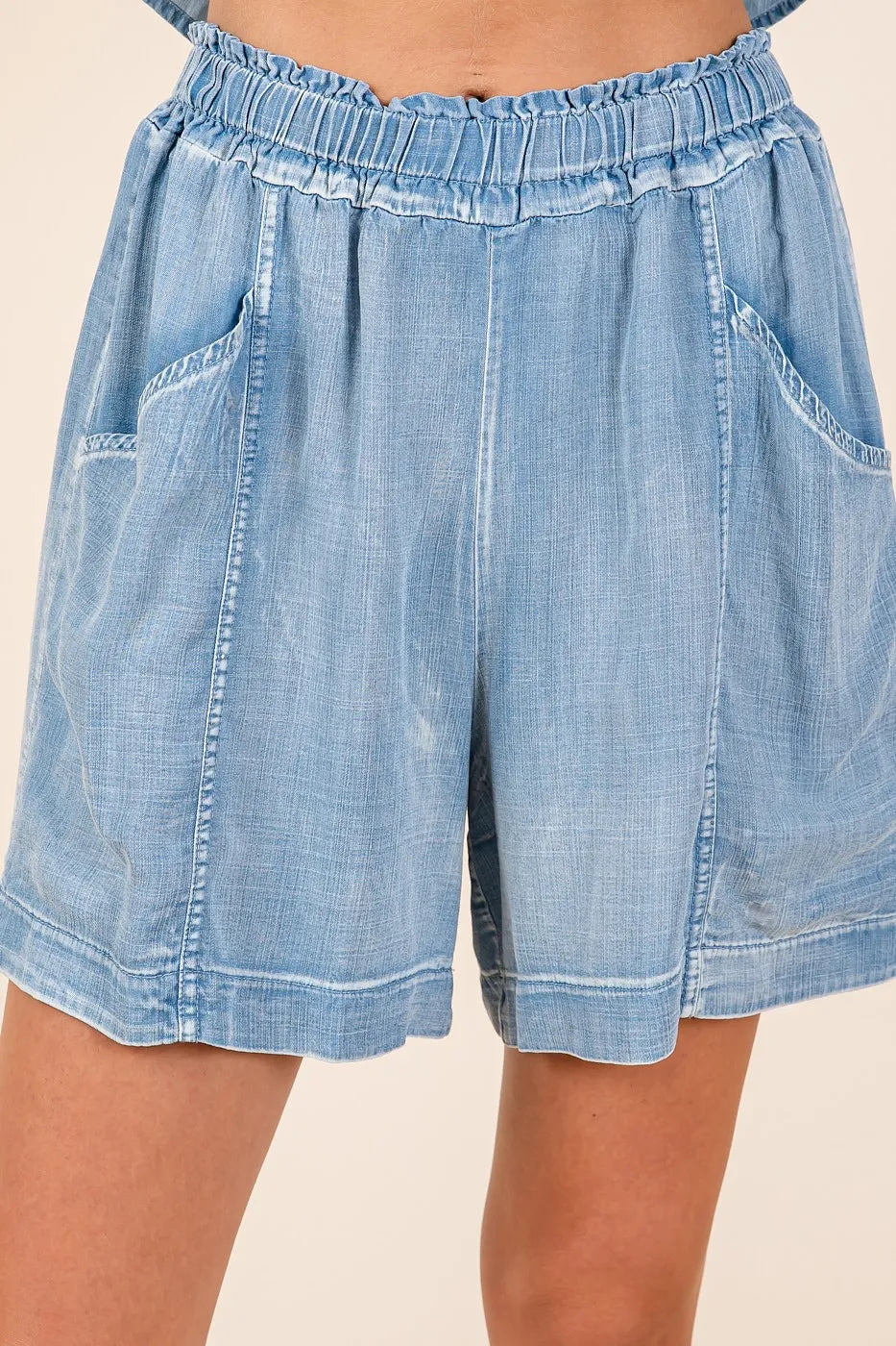Detail view of light denim chambray shorts with elastic waist and roomy patch pockets
