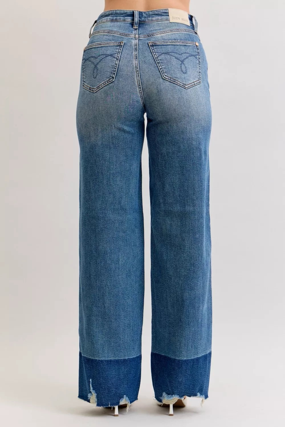 Back view: high-waist straight jeans in dark denim with stitched back pockets and raw hem