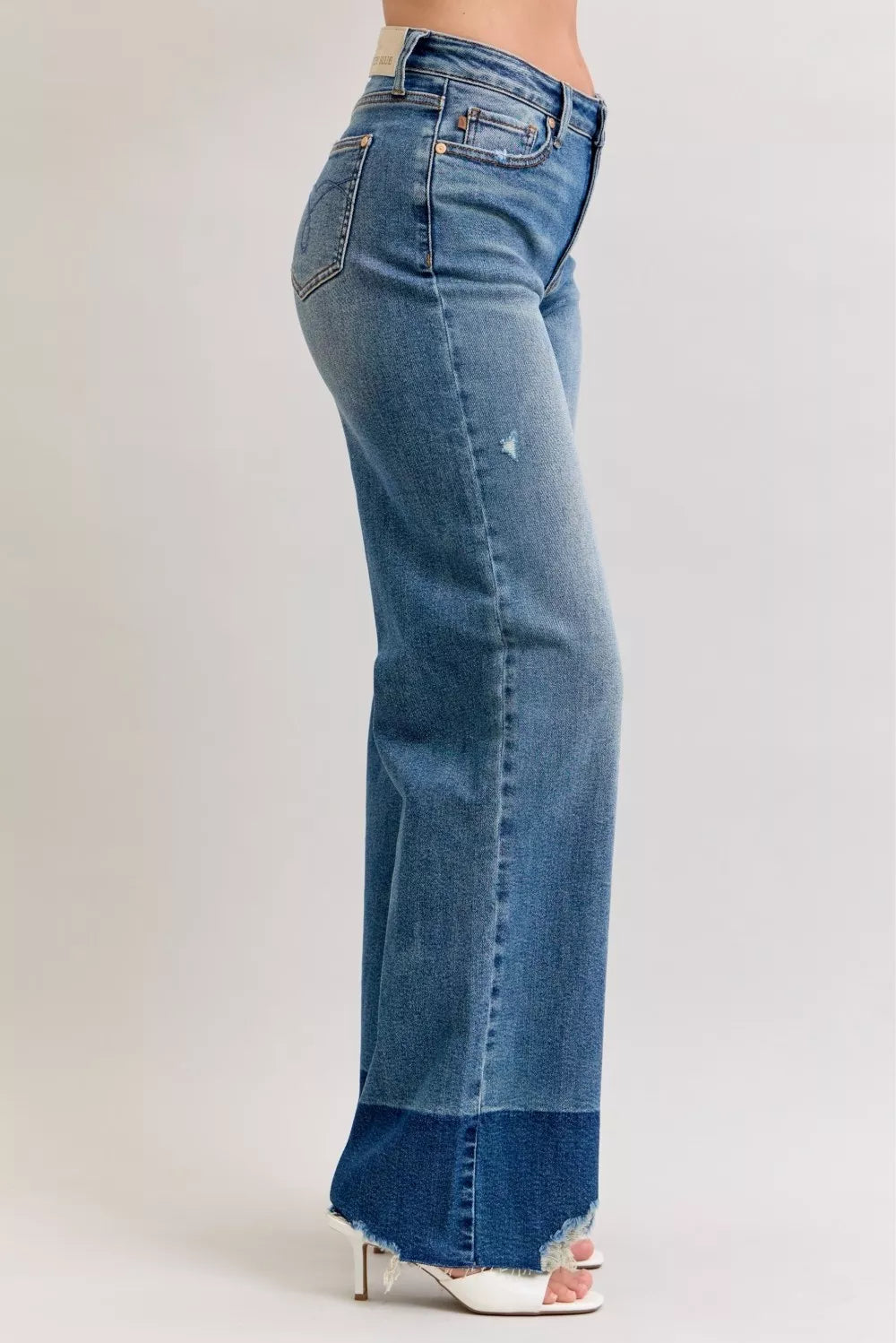 Side view of high-waist straight jeans in dark denim with raw frayed hem and belt loops