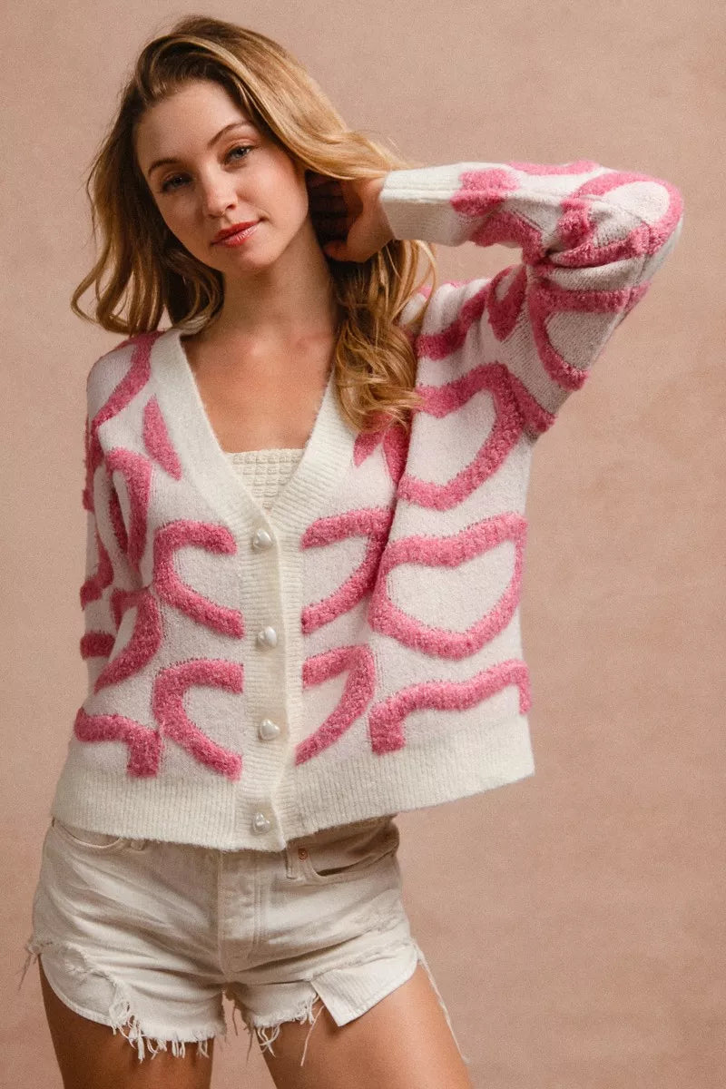 Pink heart textured cardigan with V-neck, front buttons, and long sleeves, one arm raised