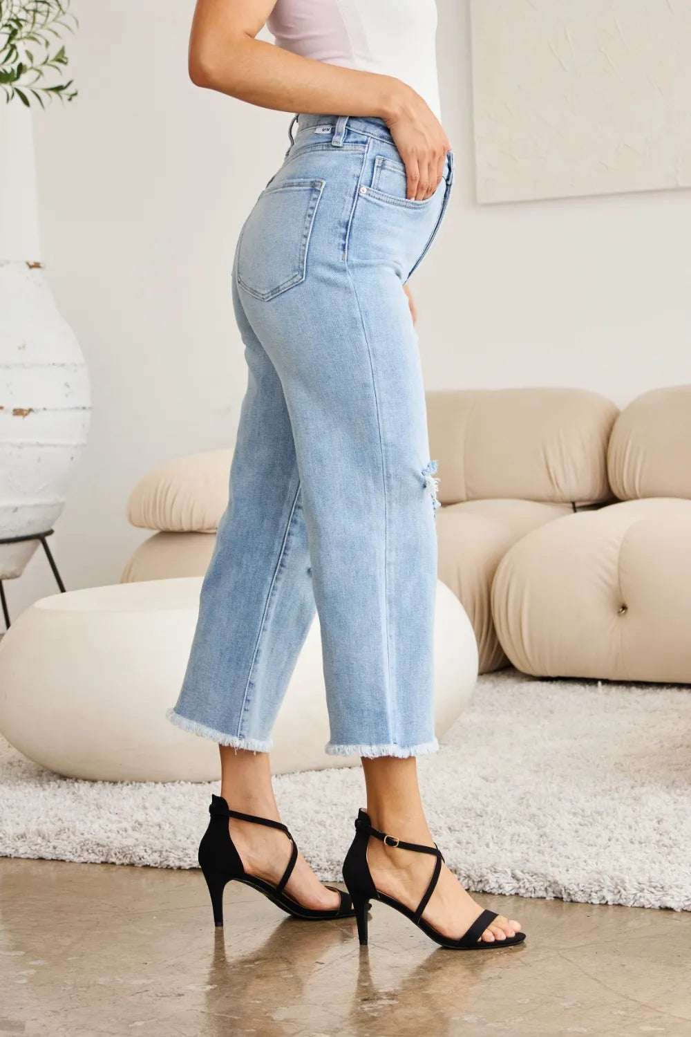 Light wash high-waist jeans with side seam detail, frayed raw cuffs, small knee rip