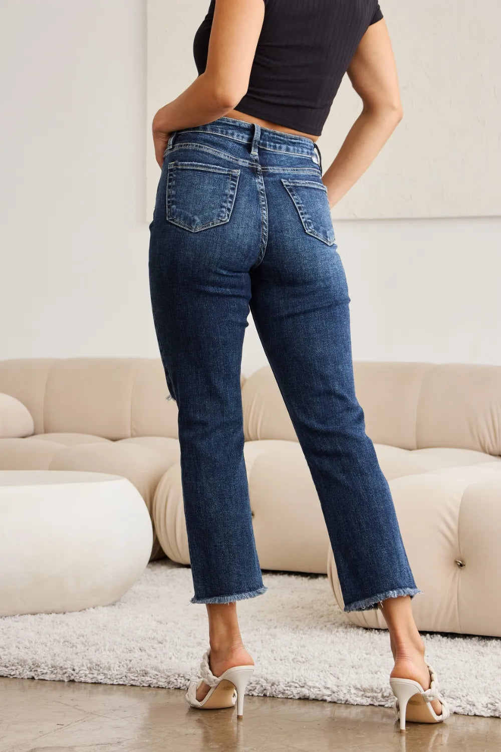 Back view: high-waist dark denim jeans with raw frayed hems