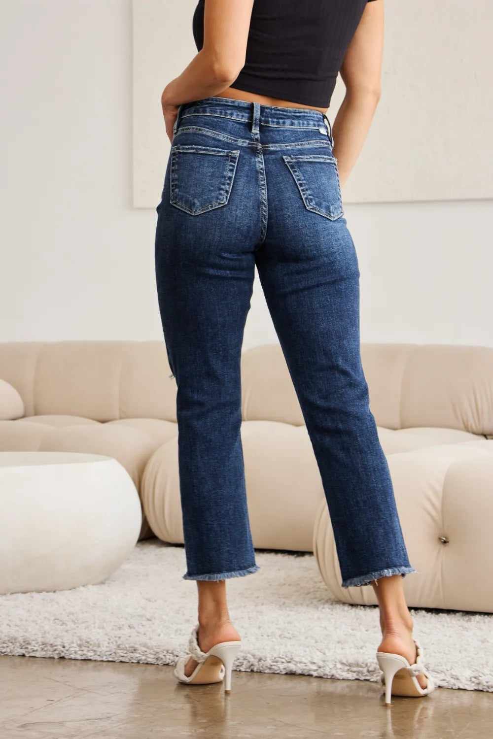 Back view of dark blue high-waist jeans with patch pockets and raw frayed hem