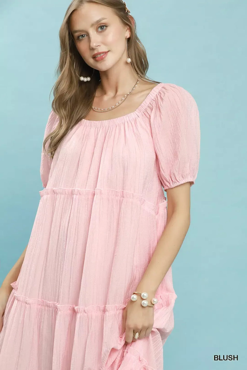 Close-up blush textured tiered midi dress with puff sleeves and pearl jewelry
