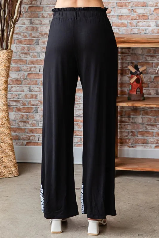 Black wide-leg pants from behind with elastic waistband and patterned hem accents