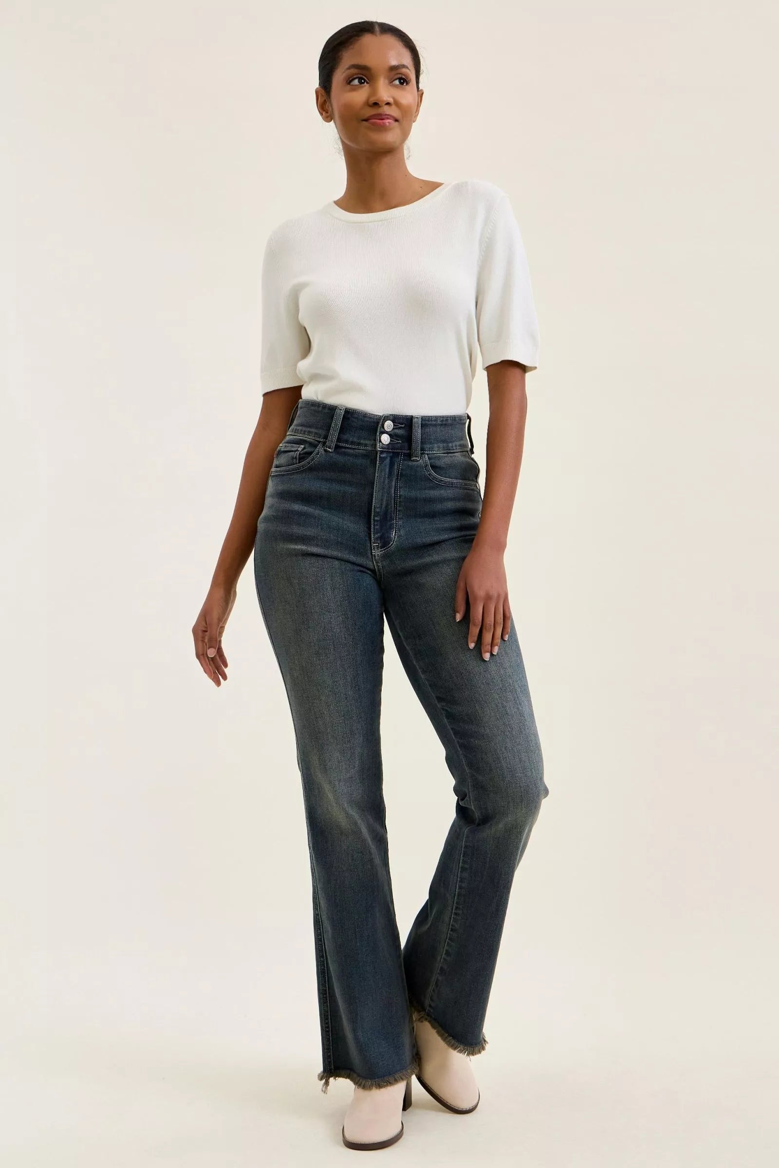 Front 3/4 view of high-waist dark denim jeans with double-button closure and frayed hem.