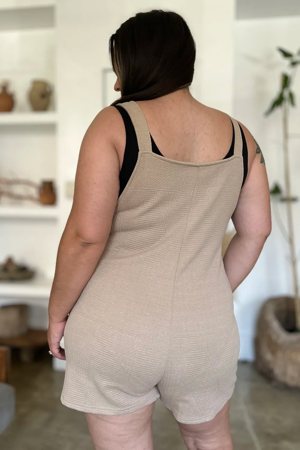 Beige textured sleeveless romper from back with wide strap crossover and short shorts