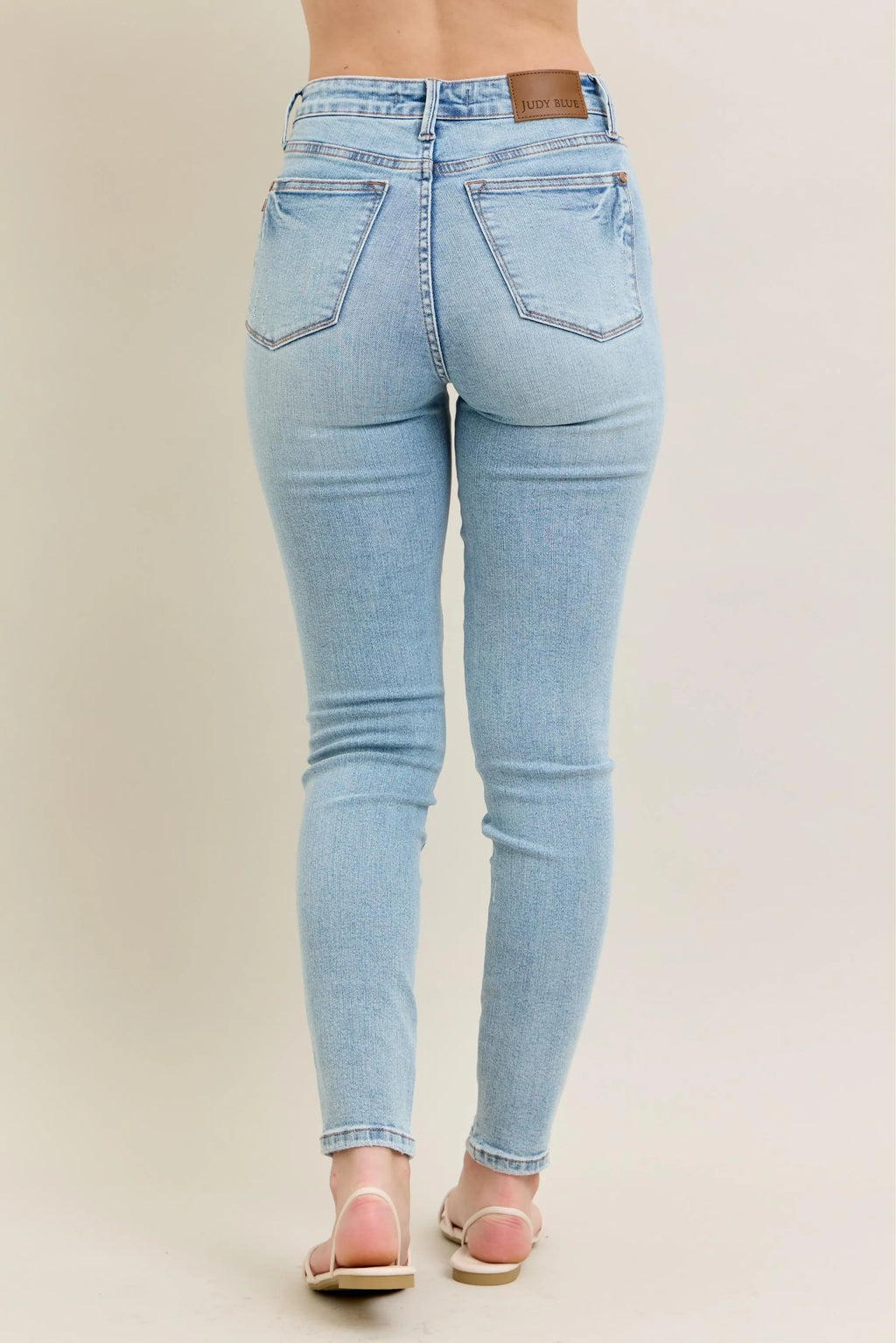 Light wash skinny jeans, back view with stitched back pockets and logo patch at waist