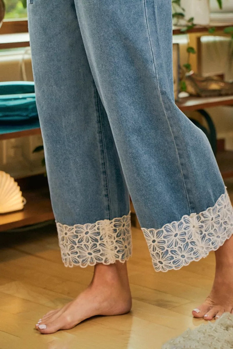 Close-up of washed denim wide-leg cuffs with flower lace trim detail and stitching