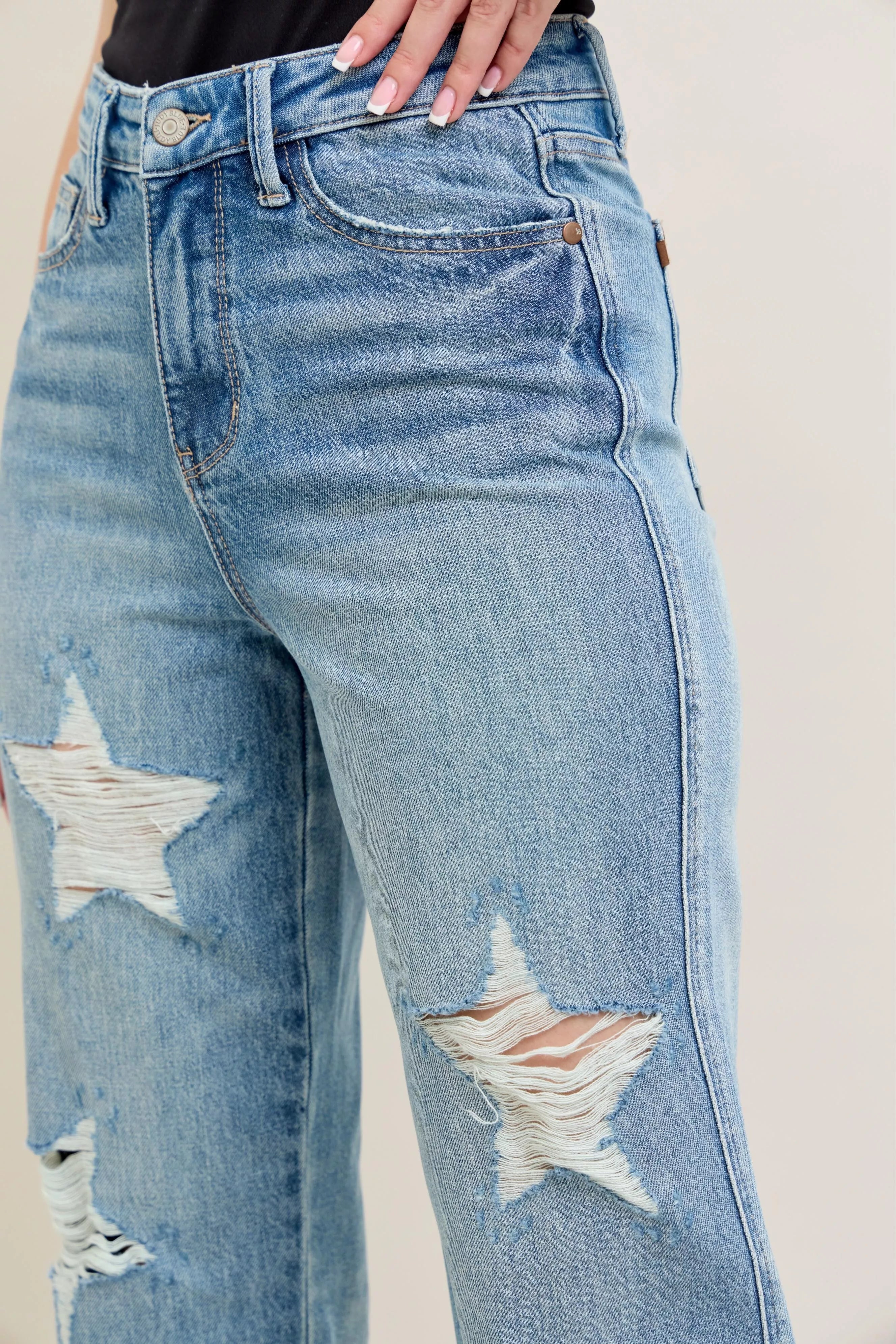 Close-up: light denim high-waist jeans with star-shaped ripped patches