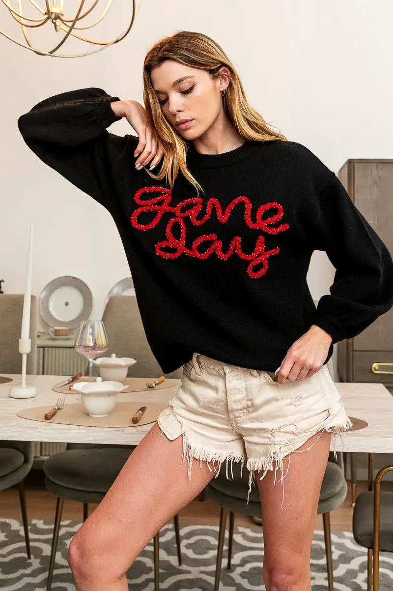 Black knit sweater with red “Game Day” text across chest, long puff sleeves