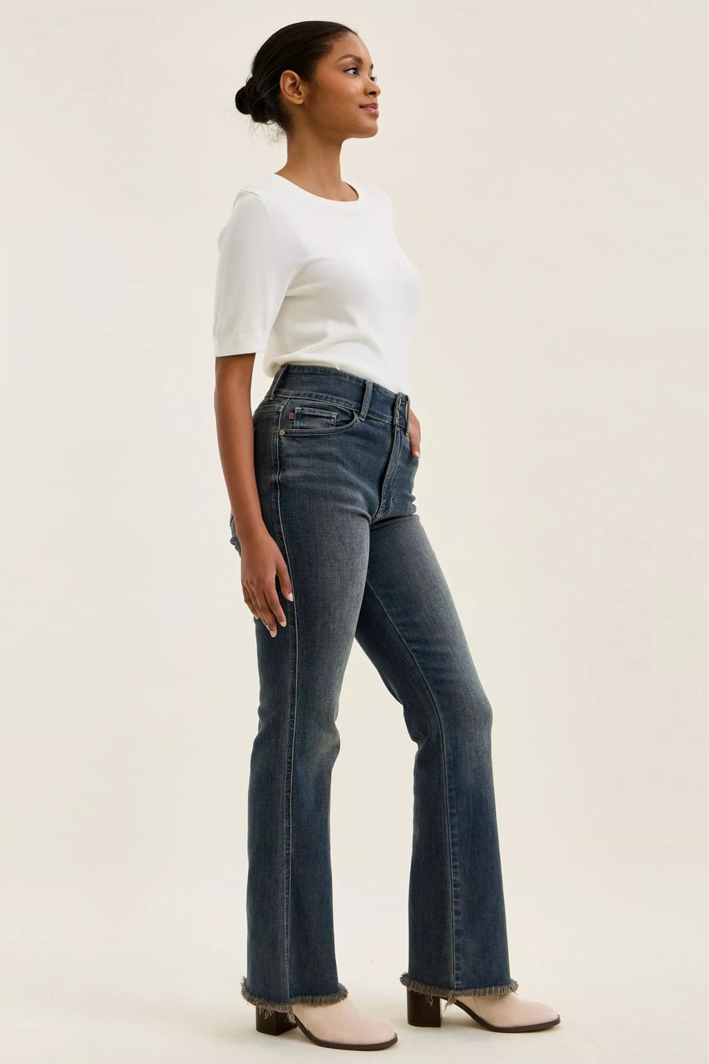 Side view of high-waist dark denim jeans with double-button front and frayed ankle hem.