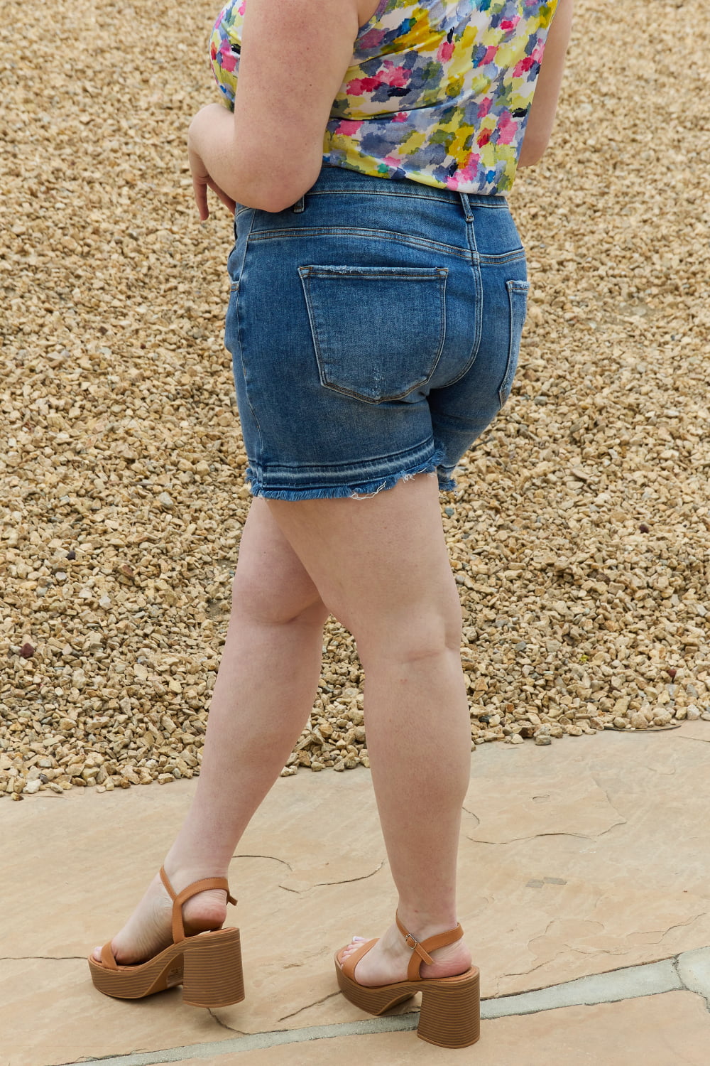 Back view of medium-wash denim shorts with frayed hem and back patch pockets