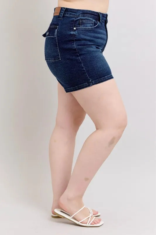 High-waist dark denim shorts, side view with flap pocket