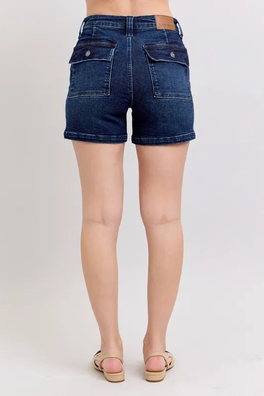 Back view: high-waist dark denim shorts with stitched seams and flap pockets