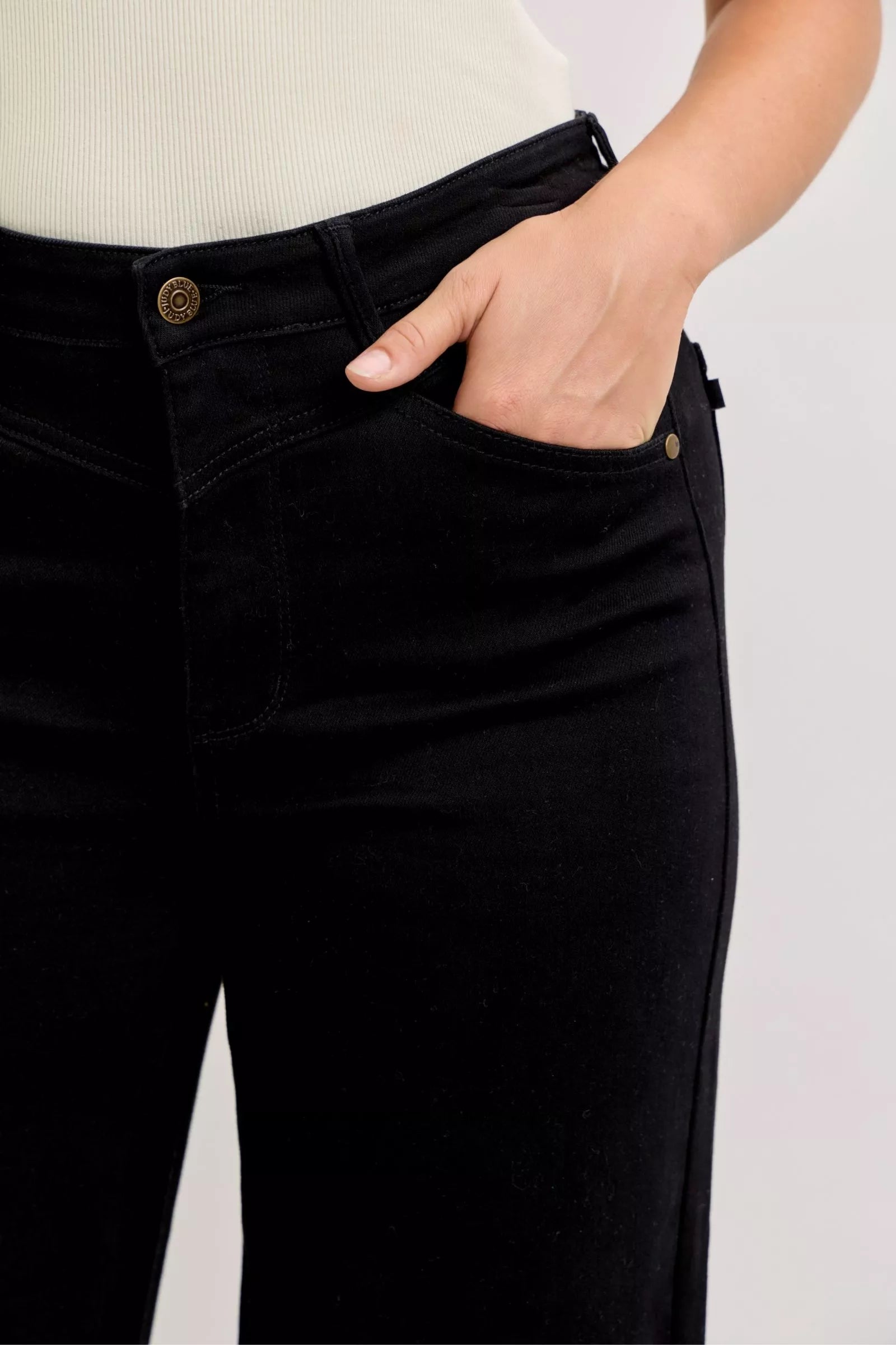 Close-up of black high-waisted jeans waistband and button detail