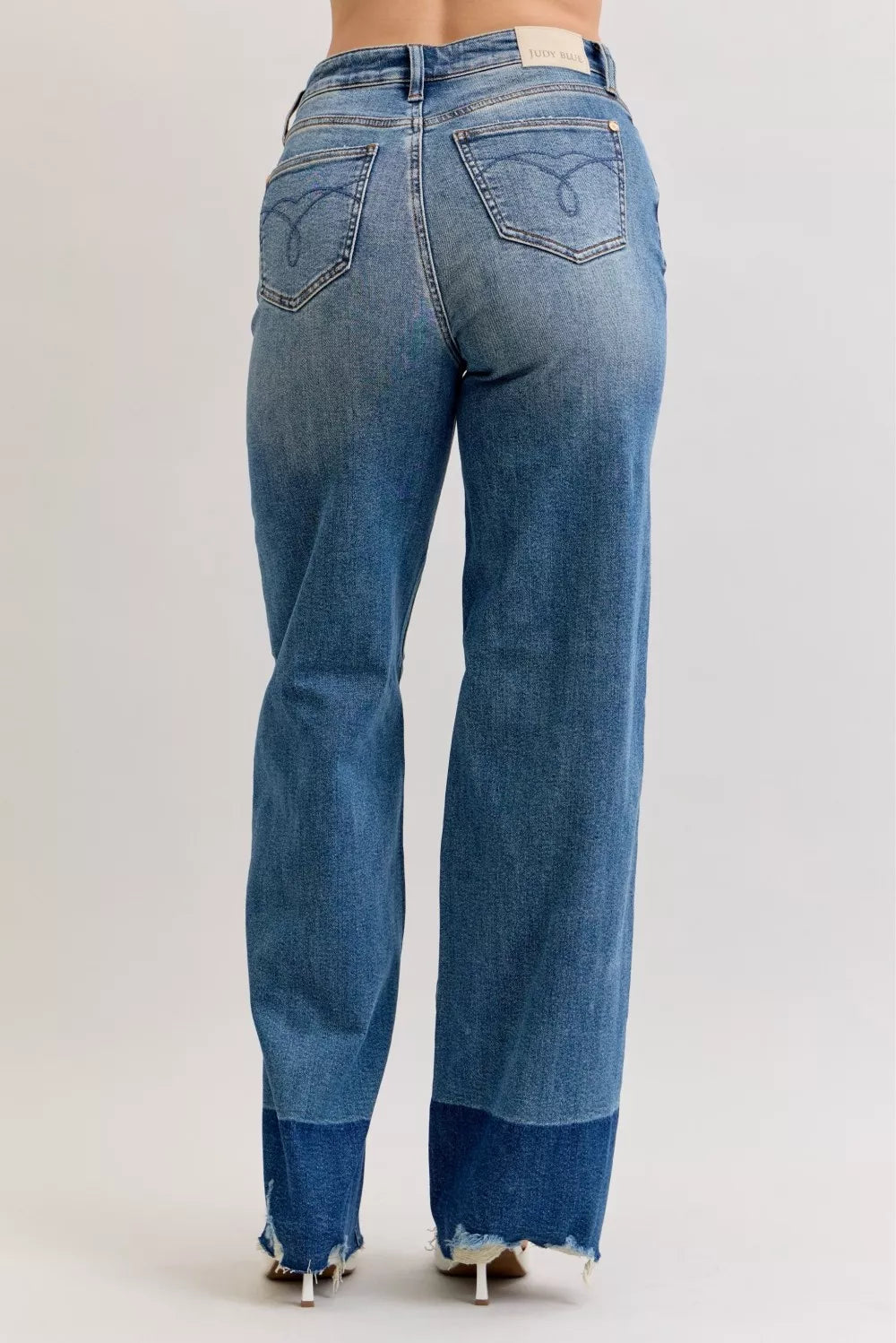 Back view of high-waist straight jeans in dark denim with raw hem and subtle whisker wash