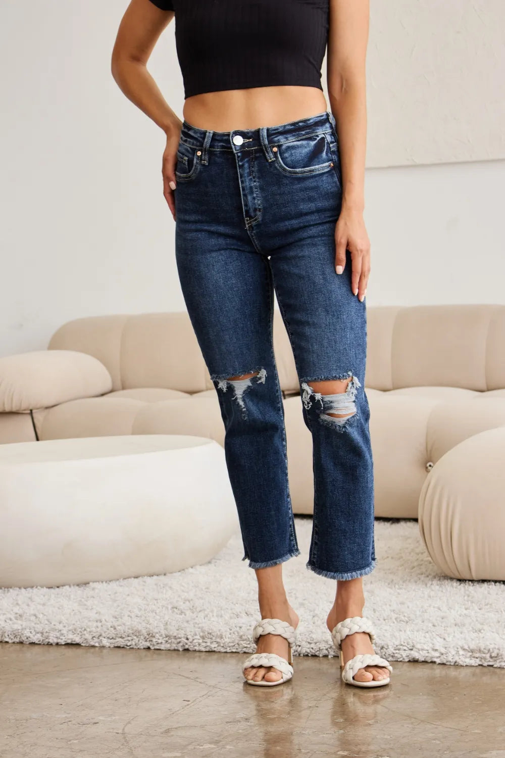 Dark blue high-waist jeans close-up: button closure, front pockets, knee distress