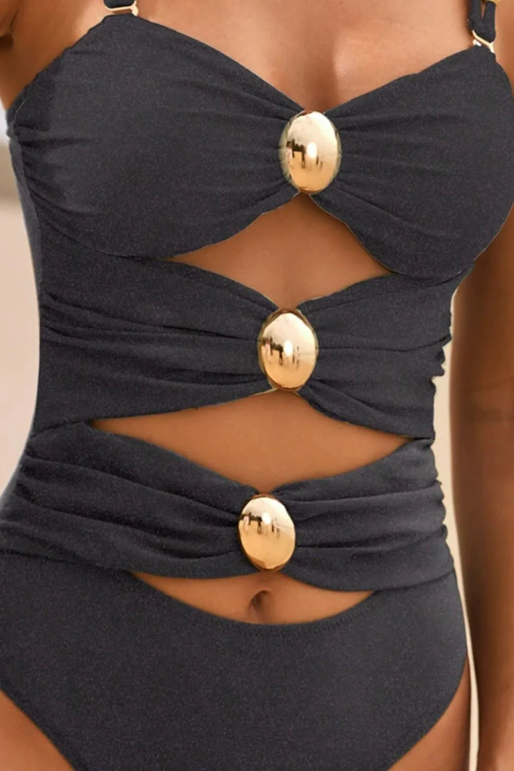 Black one-piece swimsuit detail: ruched cutout sides and gold ring buttons at bust