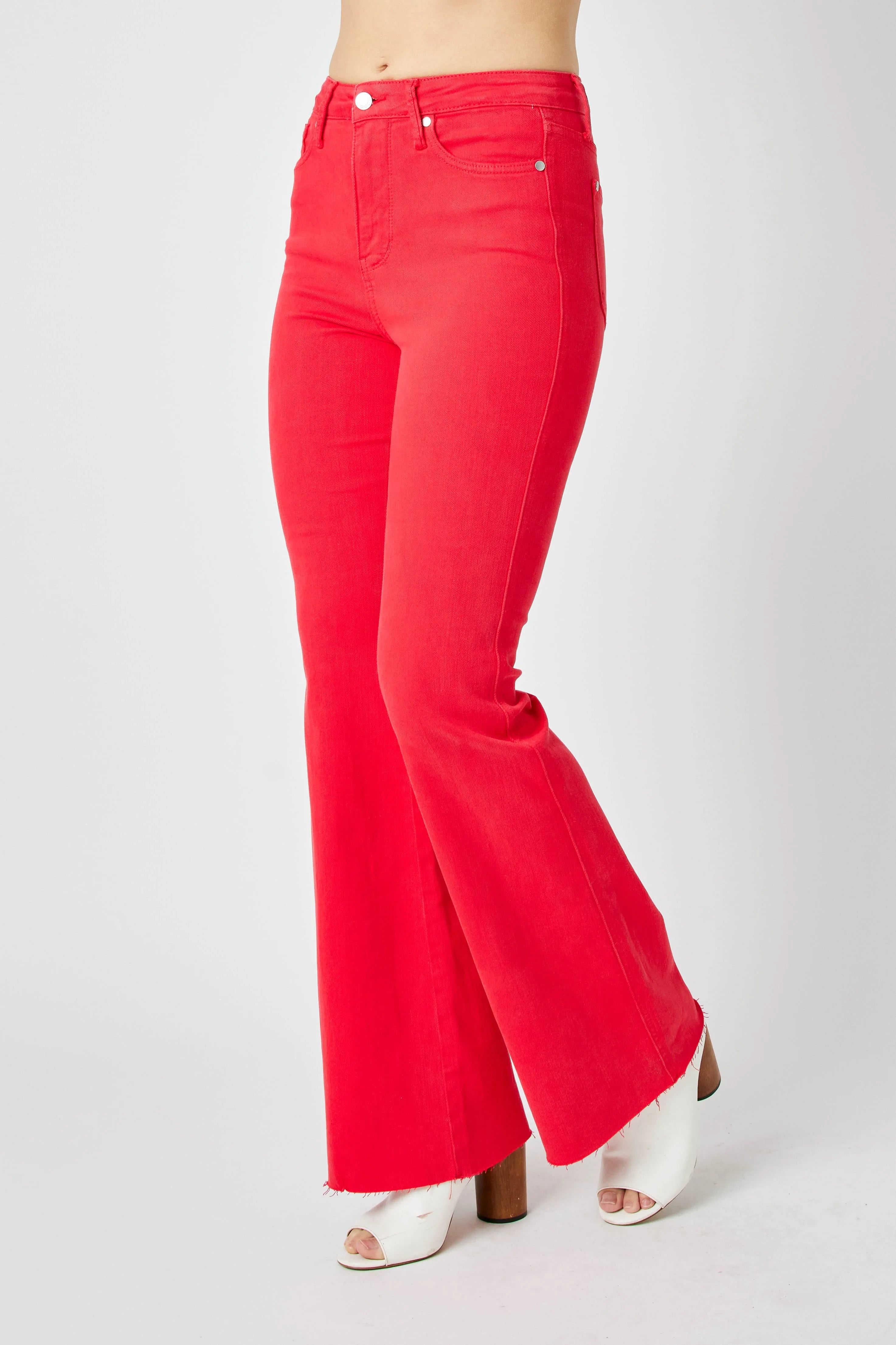 Red high-rise flare jeans on side view, wide bootcut leg opening with raw hem edge