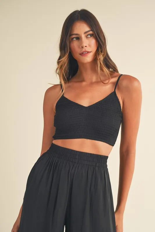 Close-up: bralette negro texturizado con tirantes finos y cintura fruncida del pantalón