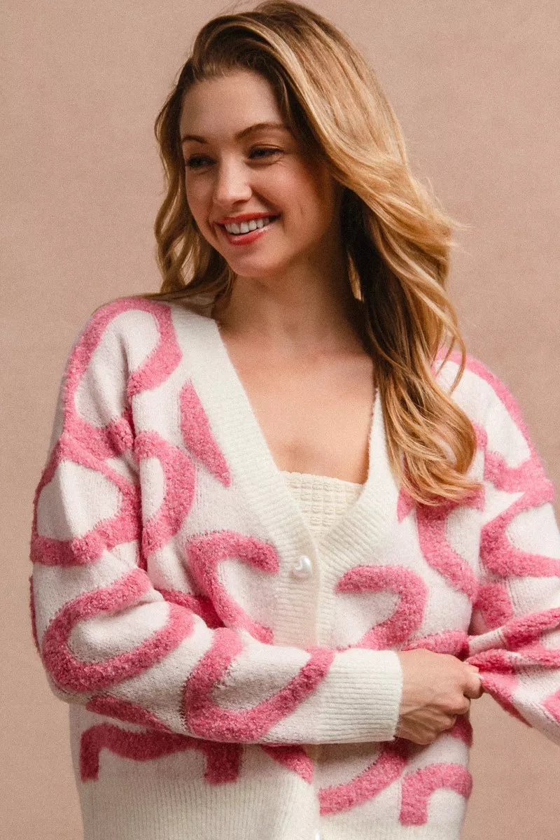 Pink-and-white textured heart cardigan with V-neck and button front, worn with sleeves down