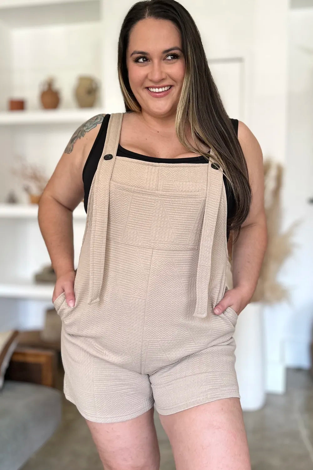 Beige textured sleeveless romper with buttoned straps and short relaxed legs