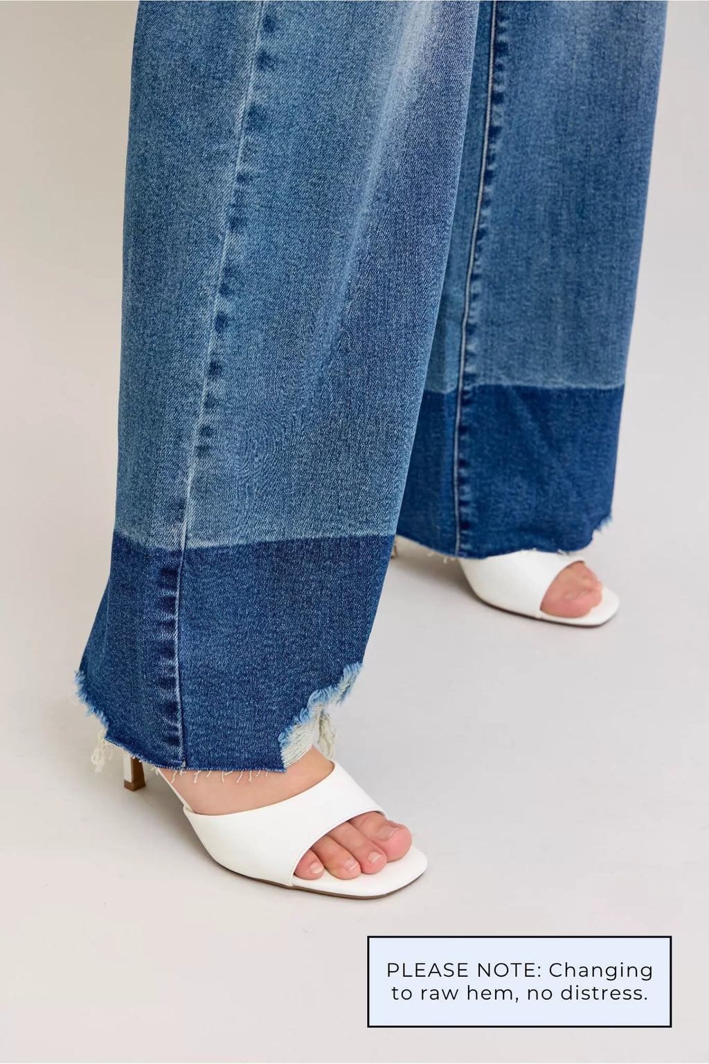 Close-up of dark denim jeans with raw hem fraying at the ankle