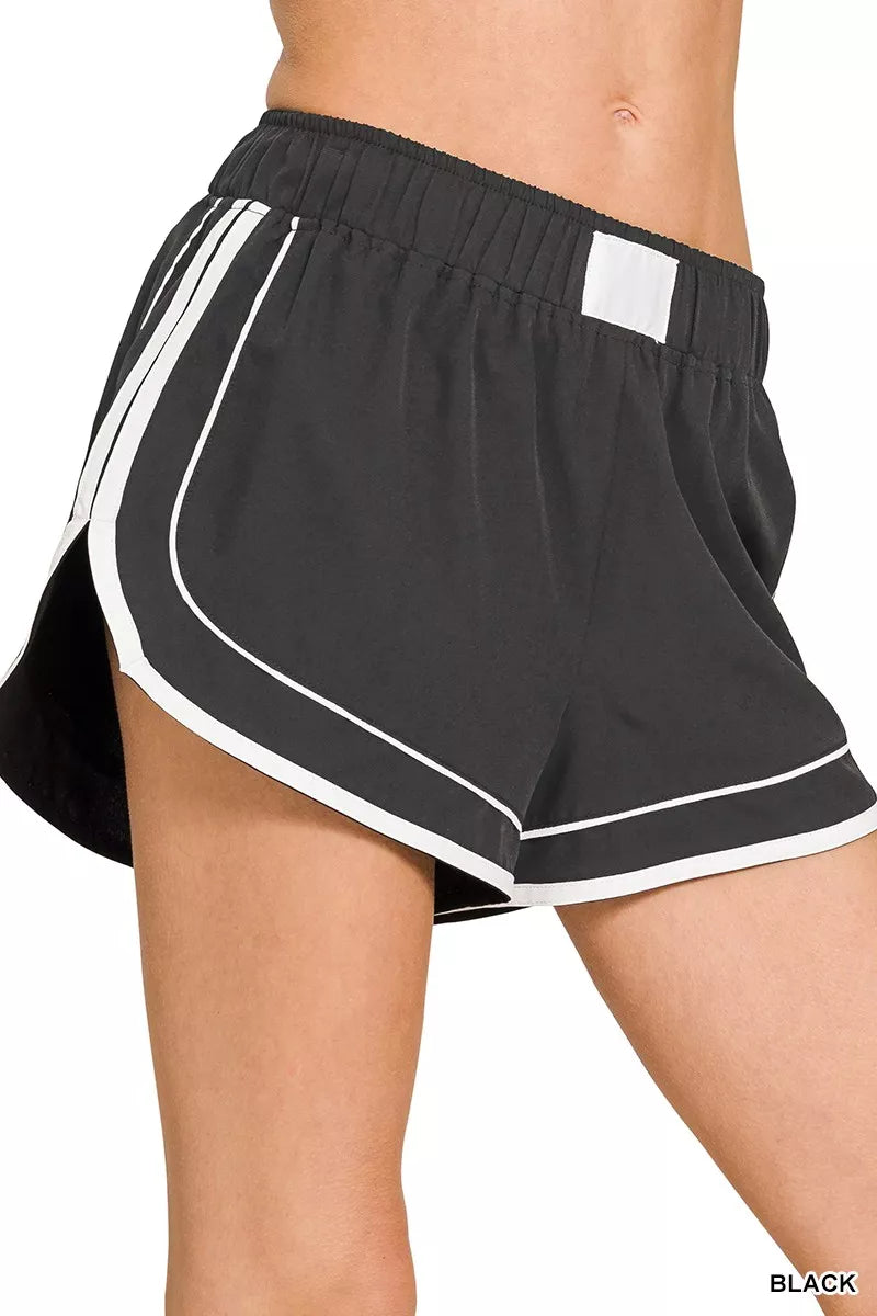 Black dolphin shorts close-up: elastic waistband and contrast white piping at hem