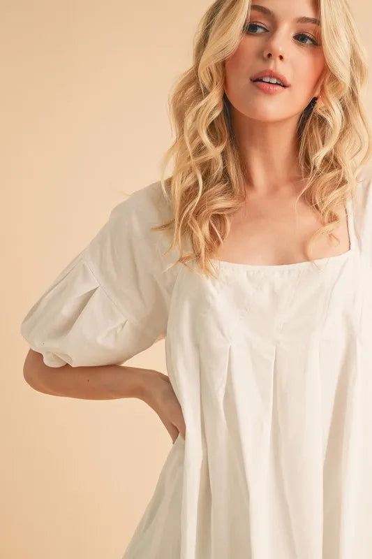 White square-neck babydoll dress with puff sleeves and pleated bodice close-up