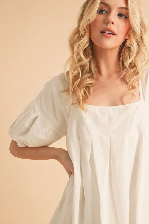White square-neck babydoll dress with puff sleeves and pleated bodice close-up