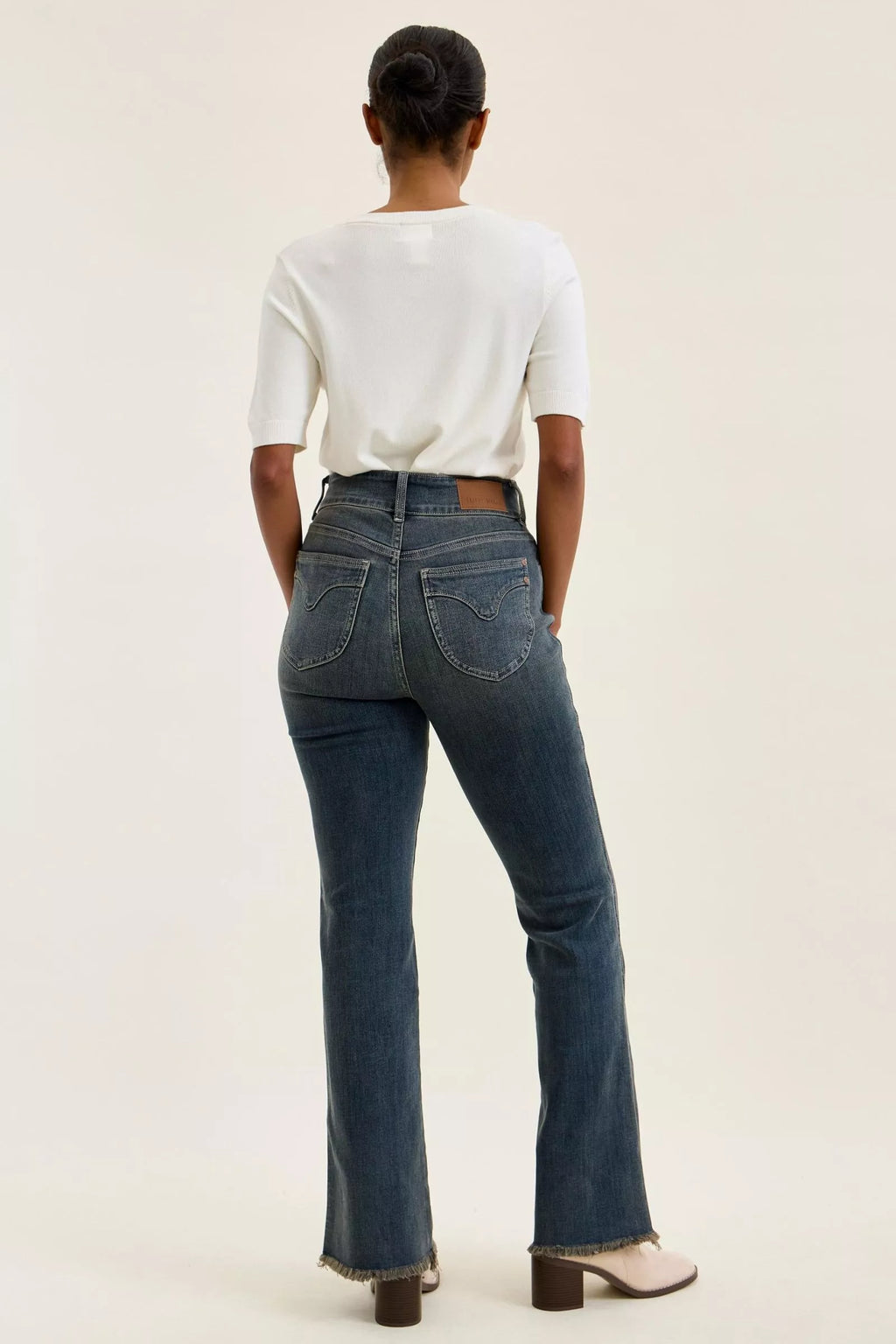 Back view of high-waist dark denim jeans with double-button front hidden, frayed hem edges.