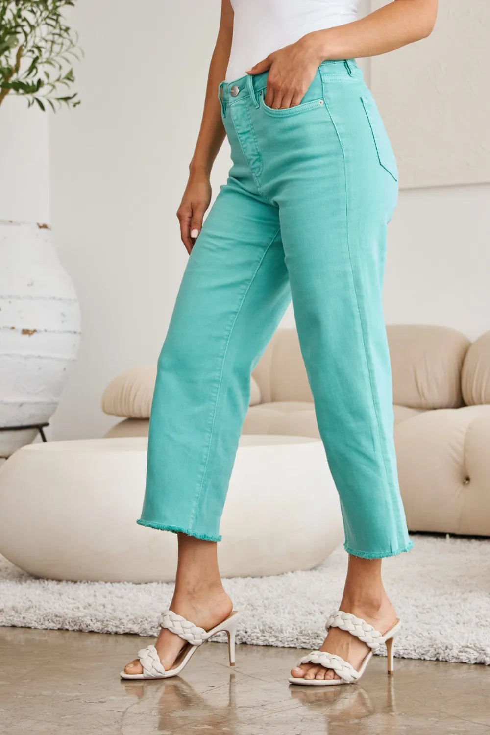 Island Green jeans close-up: front fly, belt loops, and raw hem edge