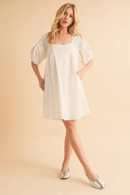 White babydoll dress with square neckline, puff sleeves, and flared hem