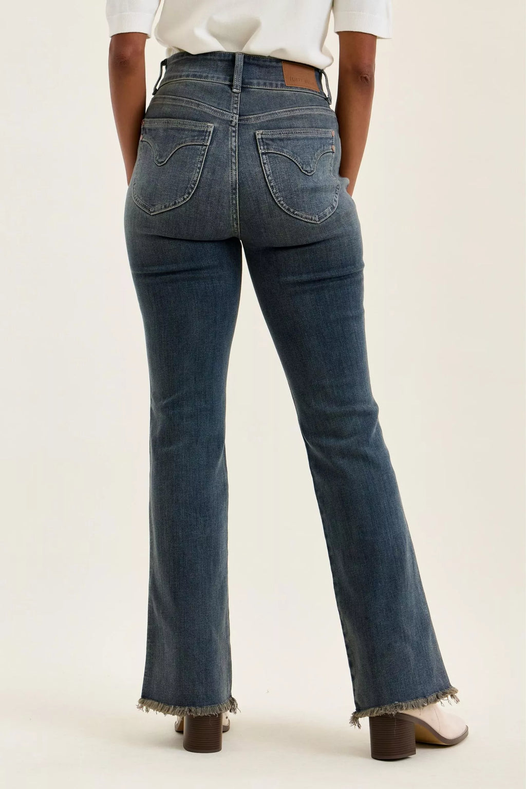 Back view of high-waist dark denim jeans with frayed ankle hem and seamed pockets.