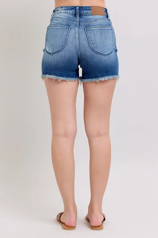 Back view of blue denim shorts with two shield-style back pockets and frayed hem